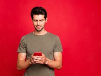 Closeup photo of amazing guy, looking interested telephone casual outfit isolated on bright red background